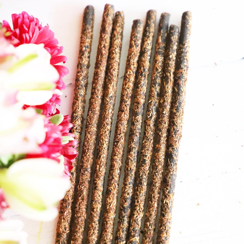 Incense stick bundle on a white background with red, white, yellow and green flowers next to it.