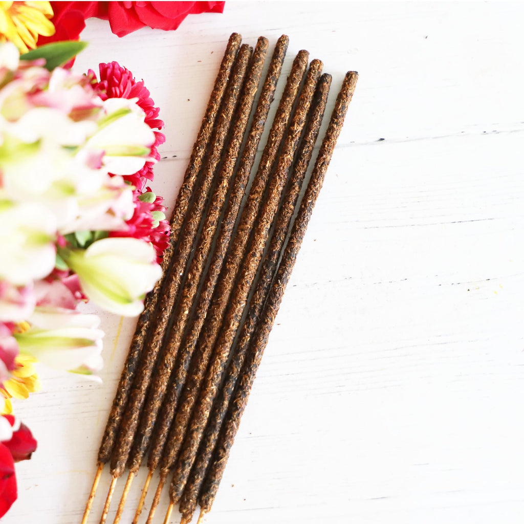 Incense sticks on white background next to pink, white and green flowers.