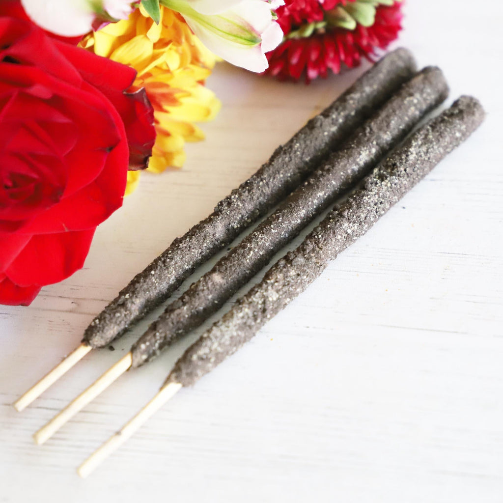 Three incense sticks on a white background with red, yellow and white flowers next to them.