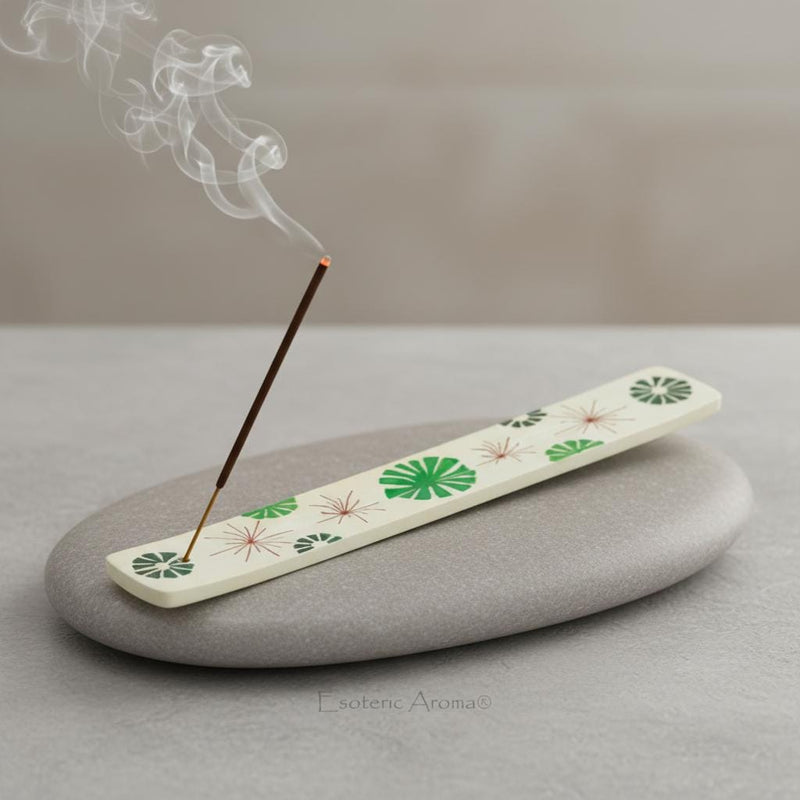 Incense holder with green and red abstract flowers on grey rock on grey table with a lit incense stick