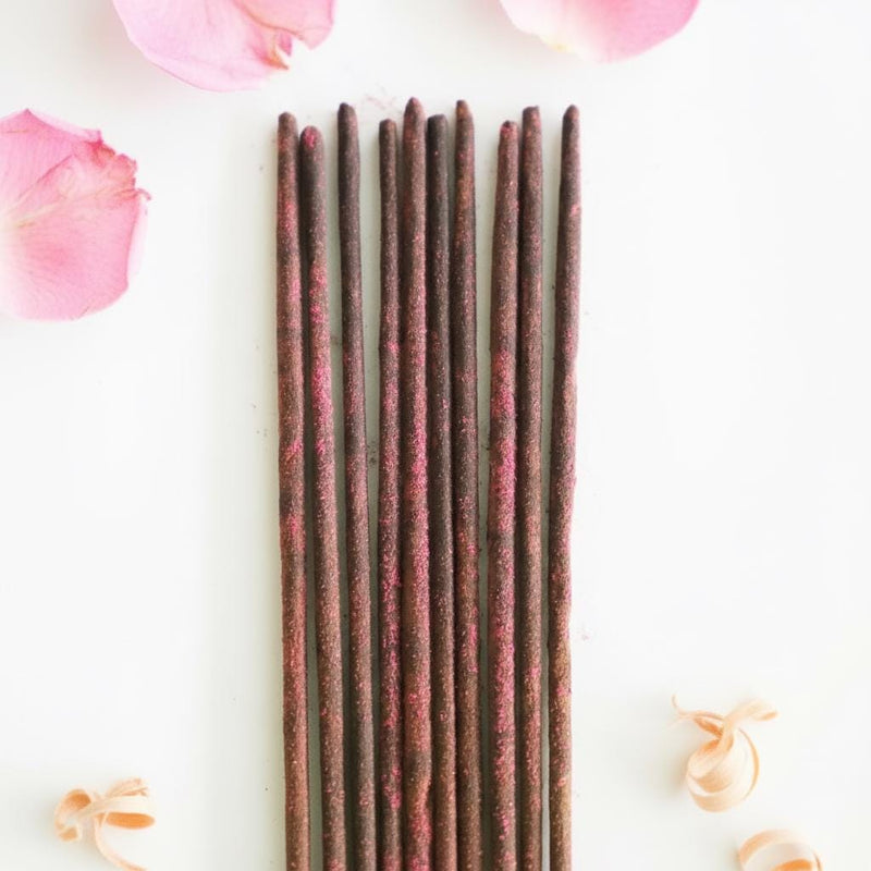 Incense sticks on a white background with pink flower petals and wood shavings.