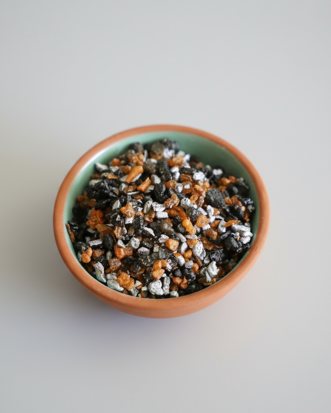 Small bowl filled with a mix of black, orange, and white resin incense grains on a light gray background