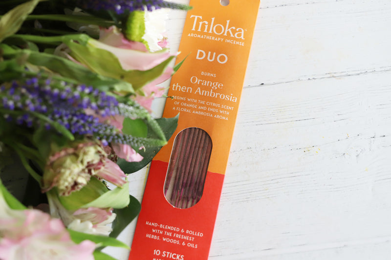 Triloka Duo Orange then Ambrosia incense packaging with flowers in the background