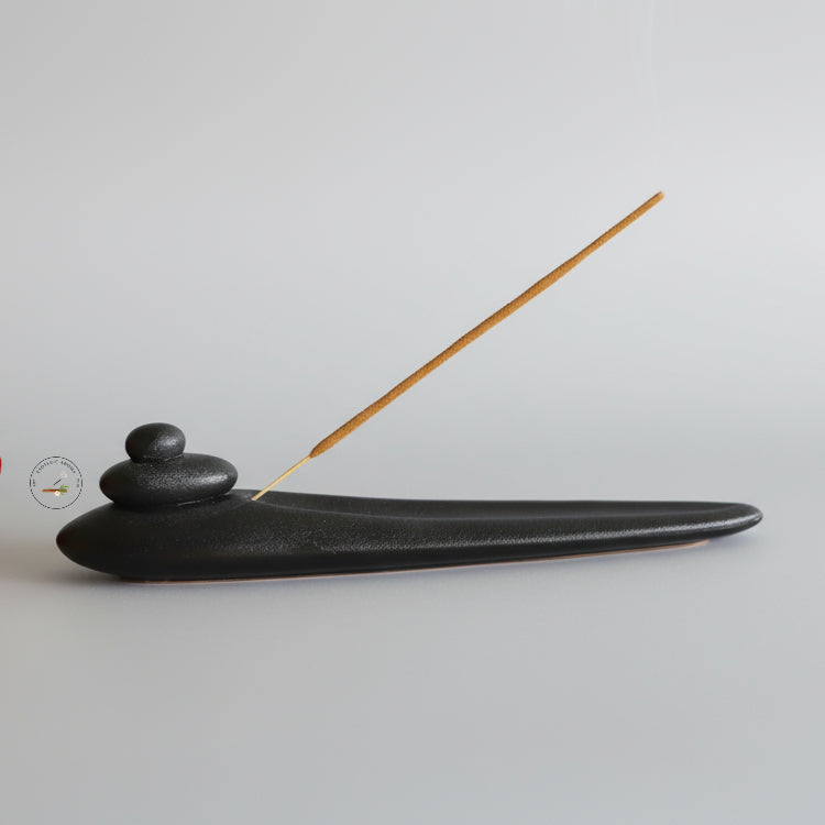 Black incense holder with a single incense stick on a light gray background